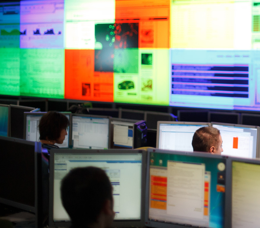 rum fullt med dataskärmar och människor som jobbar
